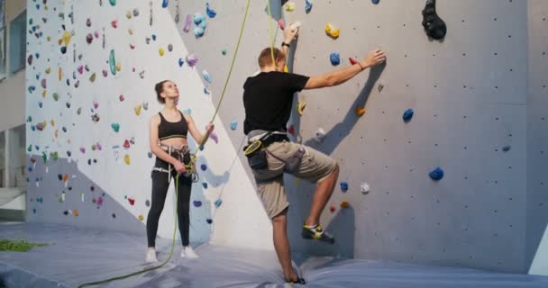 Eine junge Frau mit einem Sicherungsseil am Fuß einer Kletterwand — Stockvideo