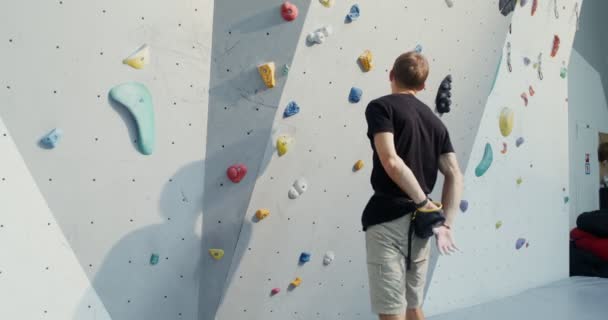 Een man behandelt zijn handen met talkpoeder en begint de klimwand te beklimmen — Stockvideo