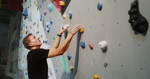 Um jovem sobe a parede de escalada interior sem cordas de segurança — Vídeo de Stock