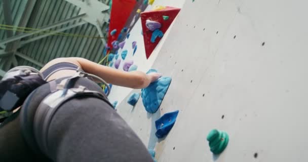 En ung idrottare klättrar upp för klätterväggen och håller fast vid de konstgjorda stenarna — Stockvideo