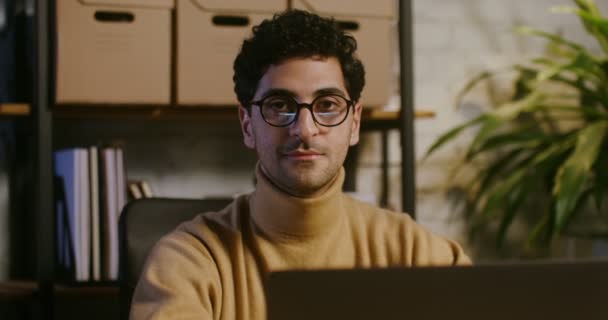 Jongeman kijkt recht in de camera terwijl hij op kantoor zit — Stockvideo