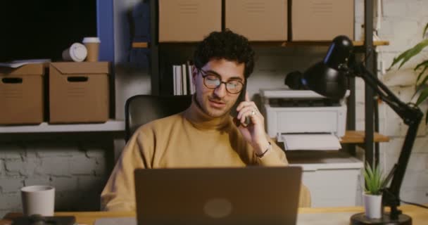 Mladý muž mluví na mobilním telefonu a používá notebook v kanceláři — Stock video