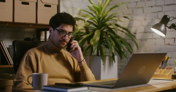 Young man talking on a mobile phone and using a laptop in office — Stock Video