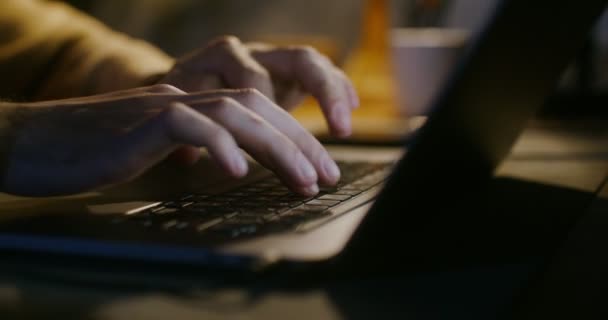 젊고 피부가 흰 남자가 전등 불빛 옆에 앉아 노트북으로 타자를 치고 있습니다 — 비디오