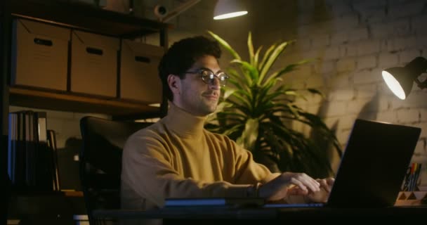 Bir adam dizüstü bilgisayarda bir video içeriyor, zevkle bakmaya başlıyor, masada oturuyor. — Stok video