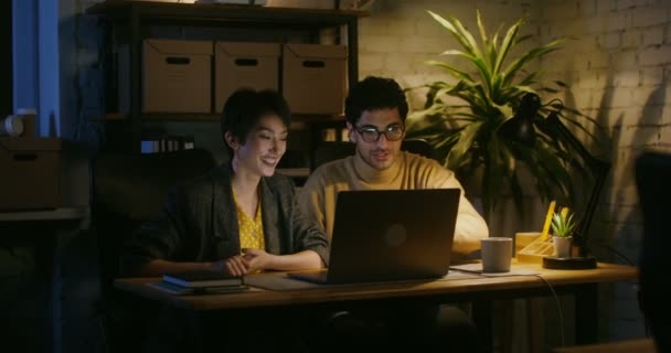 Hermosa pareja joven sentada frente a un portátil abierto hablando y riendo — Vídeos de Stock