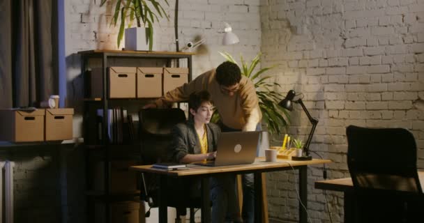 Un joven se para cerca de una mujer que trabaja en un portátil y se muestra en la pantalla — Vídeos de Stock