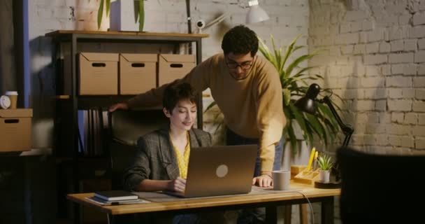 Un joven se para cerca de una mujer que trabaja en un portátil y se muestra en la pantalla — Vídeo de stock