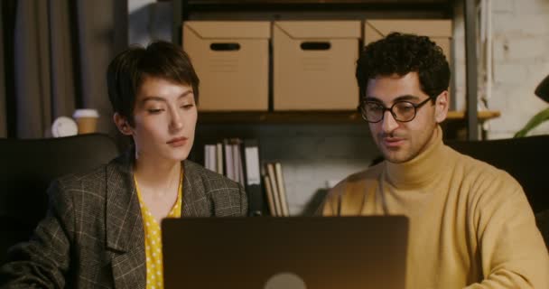 Dwóch młodych kolegów pracuje razem przy stole przed otwartym laptopem. — Wideo stockowe