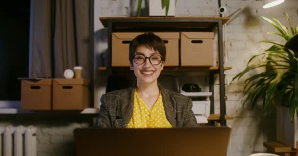 Giovane donna sorridente guardando dritto in macchina fotografica seduta di fronte al computer portatile — Video Stock