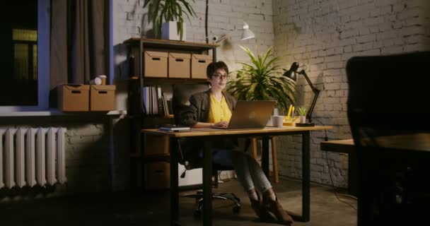 Mujer joven sonriendo mirando directamente a la cámara sentada frente a la computadora portátil — Vídeo de stock