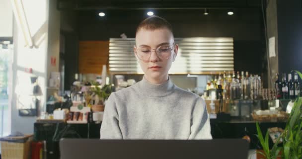 A fiatal lány laptopot használ, miközben egy modern, stílusos kávézóban ül. — Stock videók