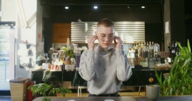 Bir kadın kulaklık takar ve kahve dükkanında bilgisayardan görüntülü sohbet başlatır.