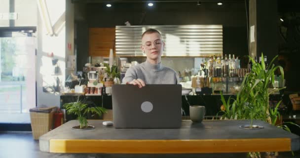 Bir kadın kulaklık takar ve kahve dükkanında bilgisayardan görüntülü sohbet başlatır. — Stok video