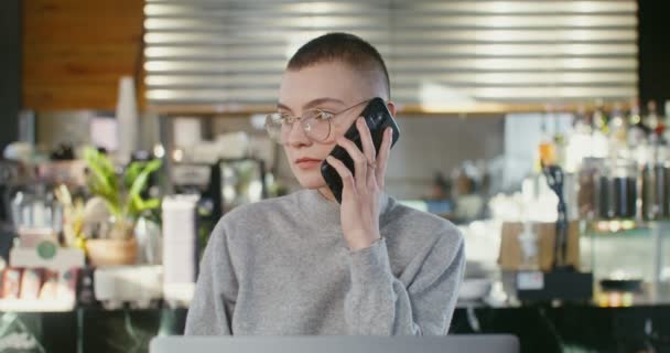 Egy fiatal nő mobilon beszél és kávét iszik egy kávézóban. — Stock videók