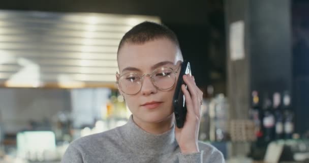 Jonge vrouw praat op een mobiele telefoon en drinkt koffie in een coffeeshop — Stockvideo