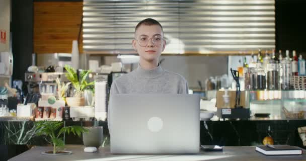 Ung kvinna tittar direkt på kameran utan att le på ett kafé — Stockvideo
