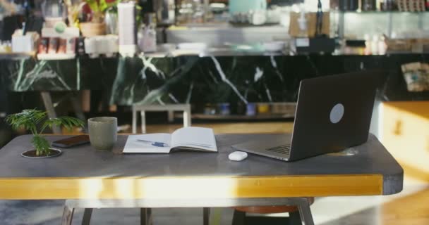 Un ordinateur portable ouvert et un bloc-notes se trouvent sur la table dans l'espace de coworking — Video