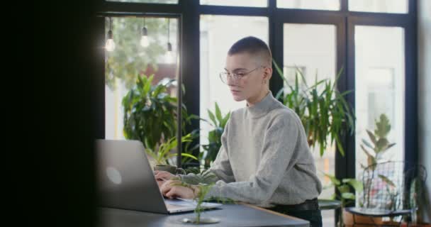 Fiatal nő jegyzetel jegyzetfüzetbe ül a laptop előtt a kávézóban — Stock videók
