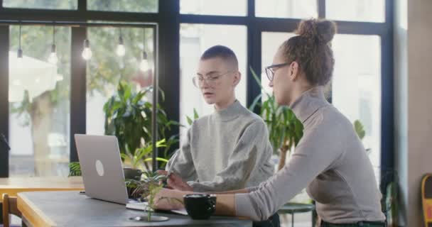 Duas jovens estudantes estudam online enquanto estão sentadas em um café moderno — Vídeo de Stock