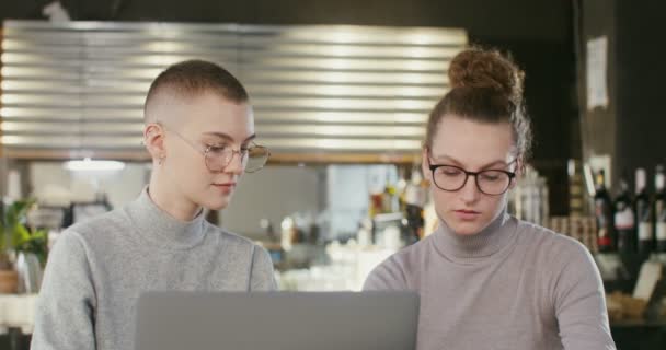 İki genç kız öğrenci, modern bir kafede otururken internetten ders çalışıyor. — Stok video