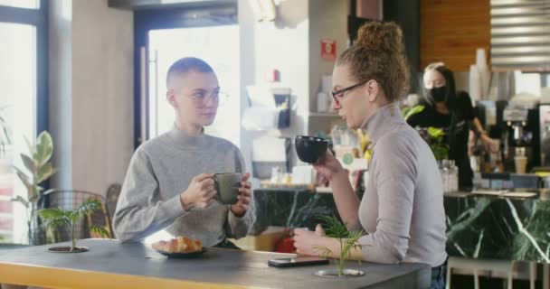İki genç kadın kahve dükkanında oturup kahve içerek sohbet ediyorlar. — Stok video