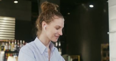 Genç bir kadın bilgisayarla konuşuyor, kafede bir masada oturuyor.