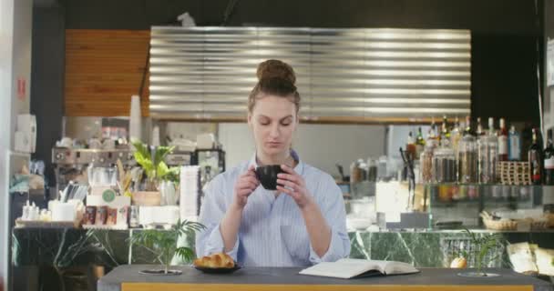 Egy gyönyörű nő könyvet olvas és teát iszik, miközben egy kávézóban ül. — Stock videók