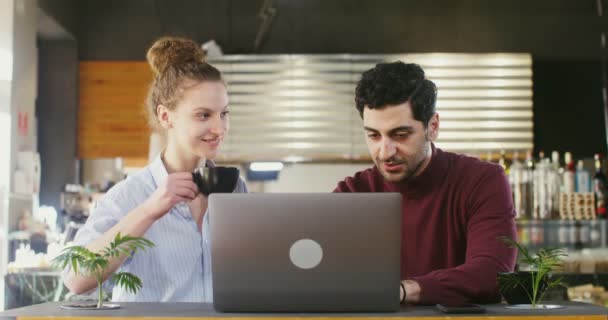 Junges Paar lächelt und spricht mit einem Laptop in einem modernen gemütlichen Café — Stockvideo