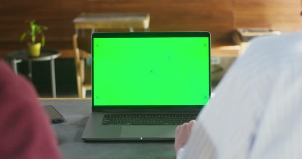 Två personer sitter vid ett bord på ett café framför en bärbar dator med en grön skärm — Stockvideo