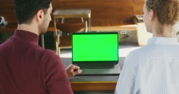 Due persone si siedono a un tavolo in un caffè di fronte a un computer portatile con uno schermo verde — Video Stock