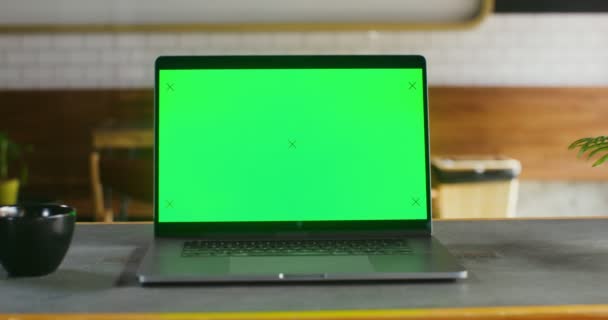 Um laptop aberto com uma tela verde fica em uma mesa em um café — Vídeo de Stock