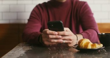 Genç bir adam bir kafede oturuyor ve telefon kullanıyor, erkek eli yakın.