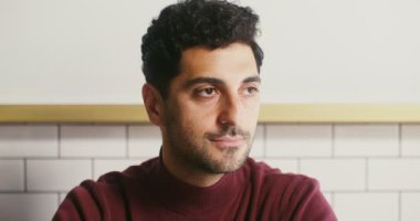 Genç siyah saçlı adam başını çevirir ve kameraya bakarak geniş bir şekilde gülümser.