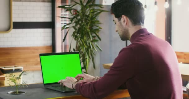 Ein junger Mann tippt in einem Café auf einem Laptop mit grünem Bildschirm — Stockvideo