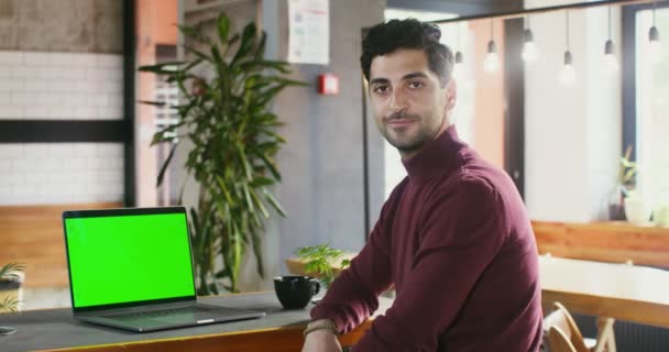 Anak muda tersenyum melihat ke kamera di depan laptop di sebuah kafe — Stok Video