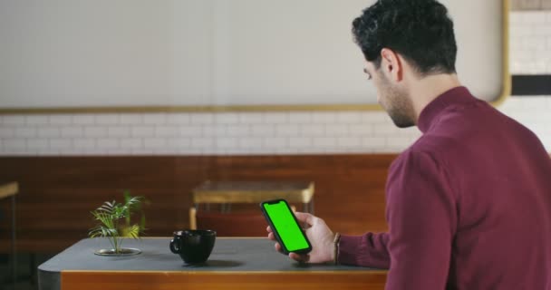 Egy férfi zöld képernyős telefont használ, miközben az asztalnál ül.