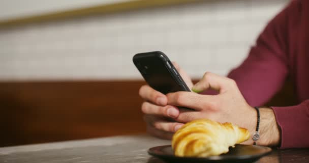 Een jonge man zit in een café en maakt gebruik van telefoon, mannelijke handen close-up — Stockvideo