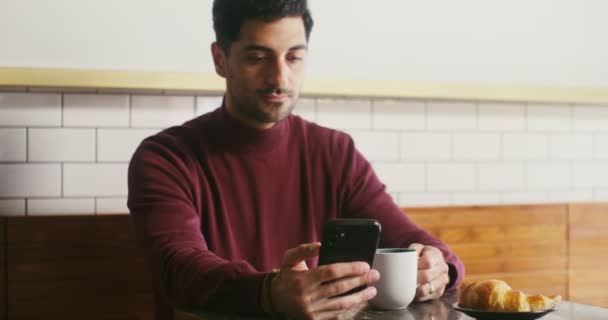 Jovem apreciando café e usando o telefone enquanto está sentado em um café — Vídeo de Stock