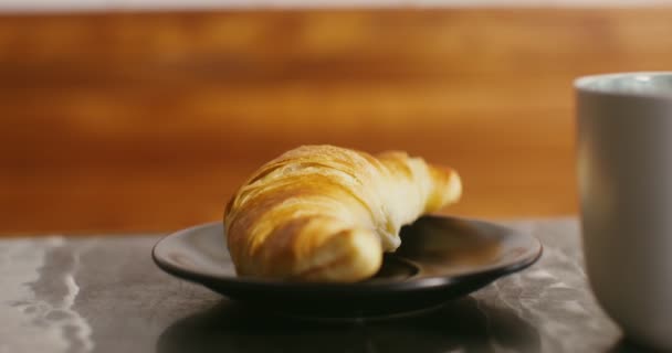 Um croissant apetitoso encontra-se em uma placa preta pequena ao lado de uma caneca, close-up — Vídeo de Stock