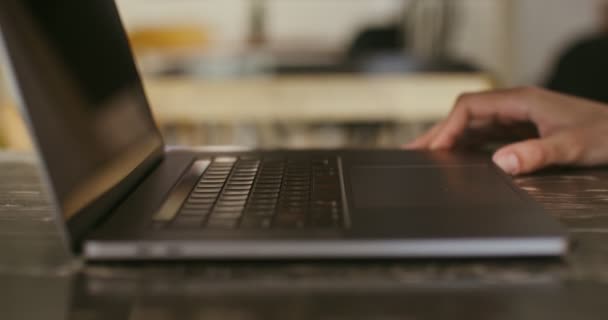 Un homme à la peau claire tape sur un ordinateur portable, assis à une table, gros plan — Video