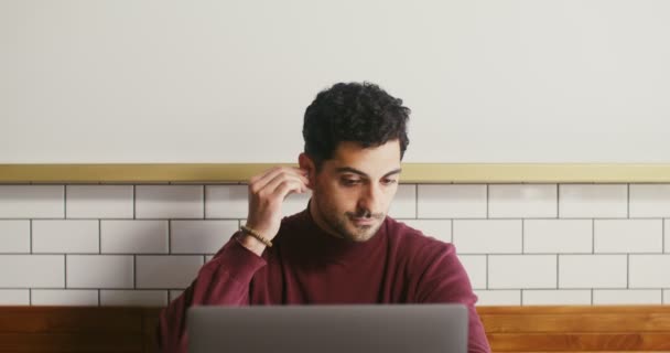 Young man inserts headphones and starts video chat on a laptop — Stock Video