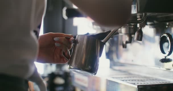 En kvinna häller varm grädde i en karaff från en kaffemaskin — Stockvideo