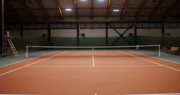 Ένα άδειο εσωτερικό γήπεδο τένις με πορτοκαλί ελαστικό κάλυμμα και τεντωμένο δίχτυ — Αρχείο Βίντεο