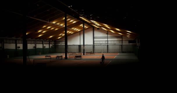 Um homem está andando com uma raquete e uma cesta cheia de bolas de tênis em suas mãos — Vídeo de Stock