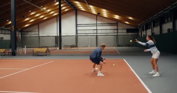 A man and woman throwing tennis balls to each other, hitting them on the floor — Stock Video