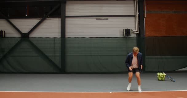 Молодой человек делает разминку, прежде чем играть в теннис на крытом теннисном корте — стоковое видео