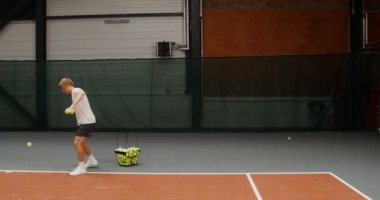 Genç bir adam kalenin üzerinden raketle tek tek tenis topları atıyor.