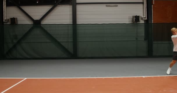 Un joven lanza pelotas de tenis con una raqueta sobre la red una por una — Vídeos de Stock