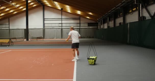 Un joven lanza pelotas de tenis con una raqueta sobre la red una por una — Vídeos de Stock